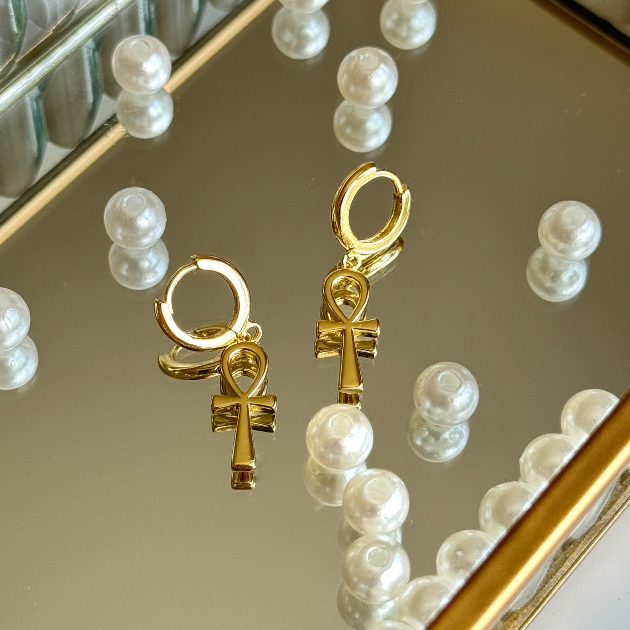 Picture of ankh earrings placed on a mirror tray with beads scattered around 