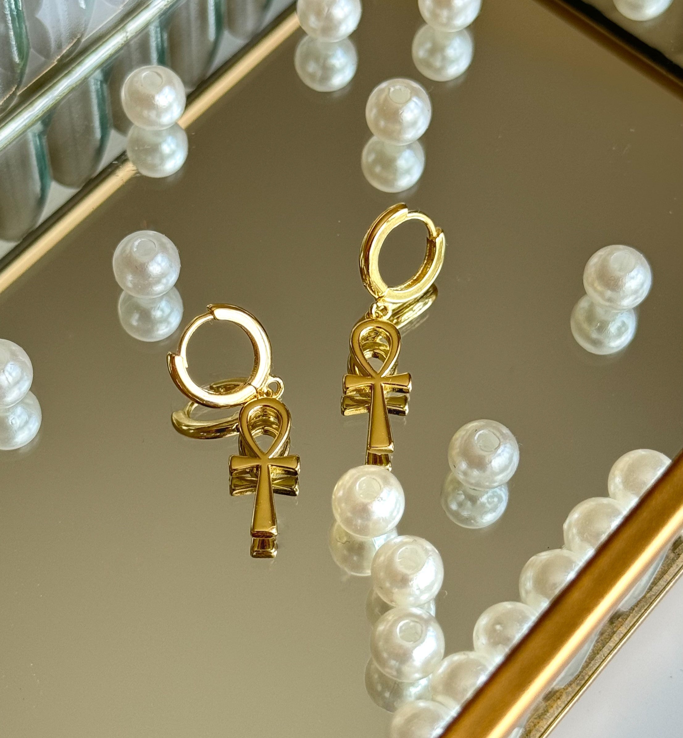 Picture of ankh earrings placed on a mirror tray with beads scattered around 