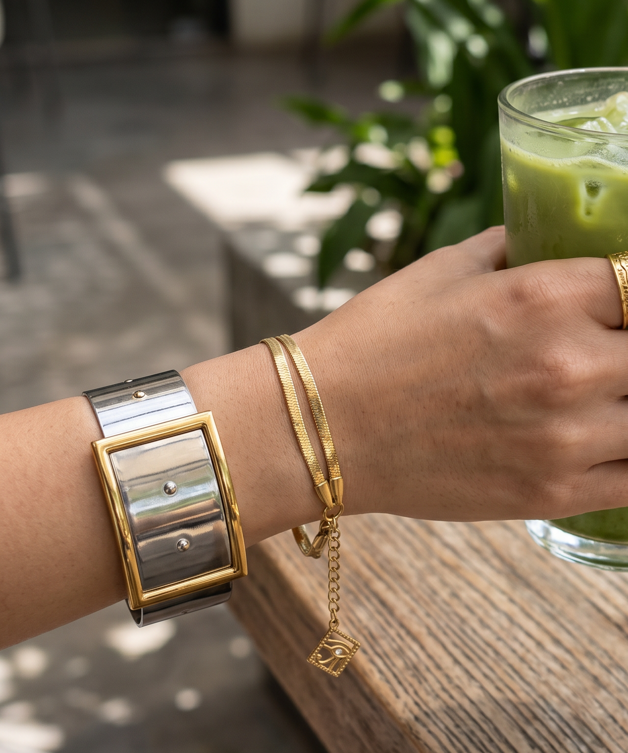 Hand holding a glass of green drink with a watch and bracelet on a wooden surface