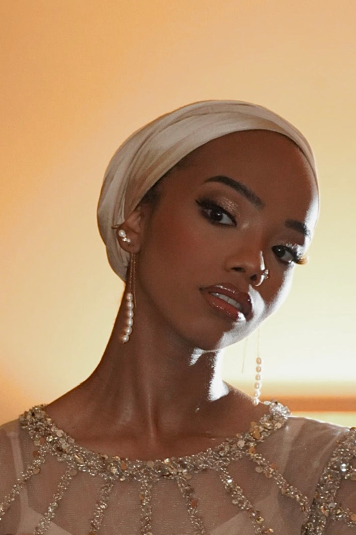 Woman wearing a headscarf and beaded top against a warm-toned background