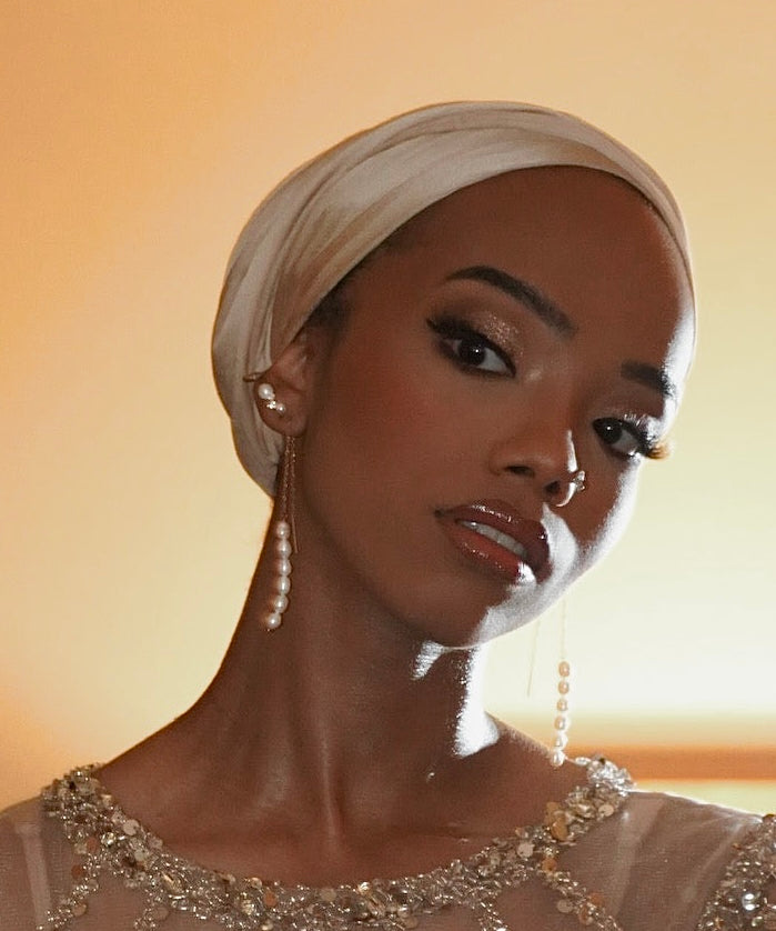 Woman wearing a headscarf and beaded top against a warm-toned background