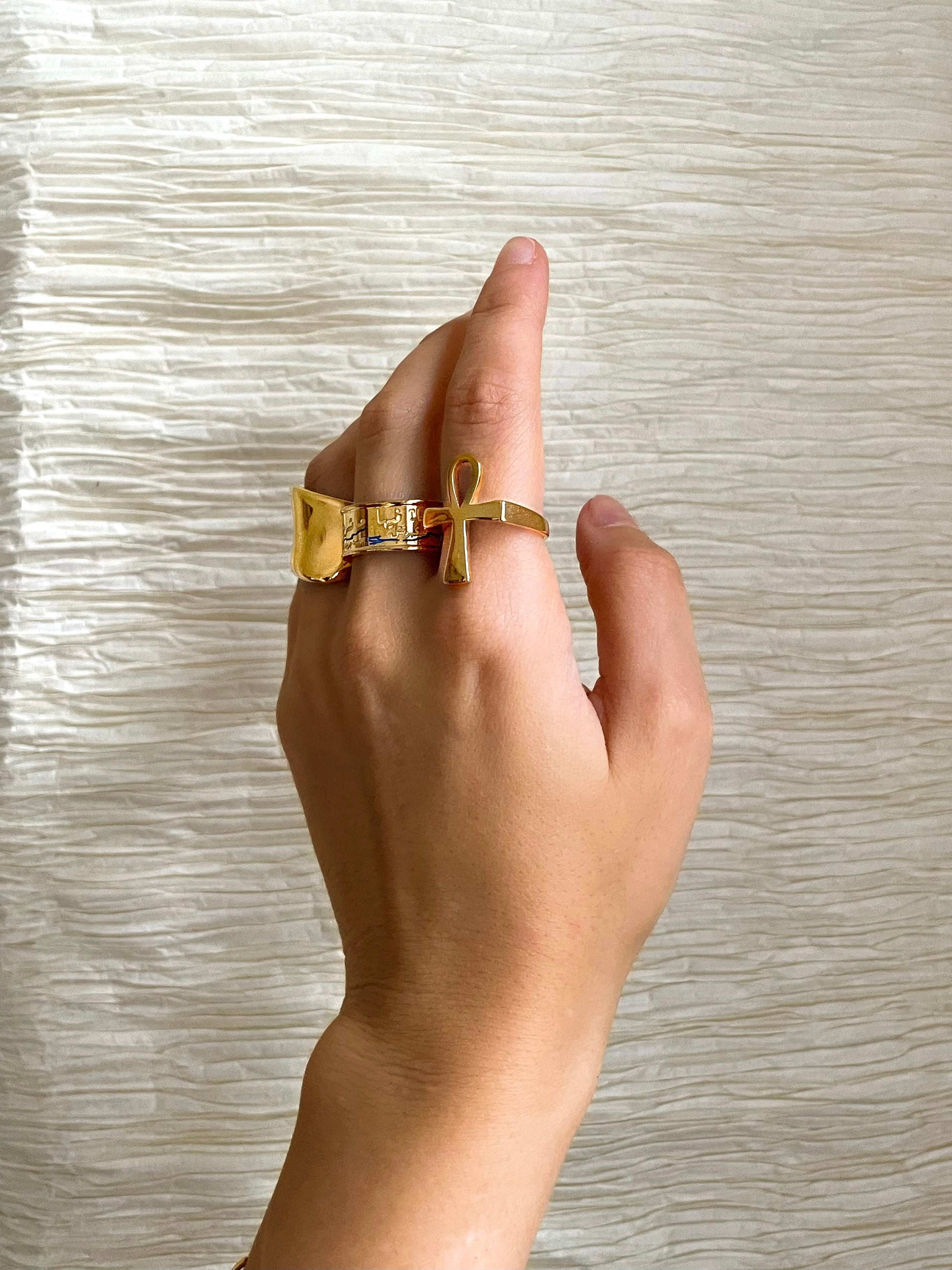 Gold Egyptian Ankh statement ring worn on a hand against a textured background by KIRO UK