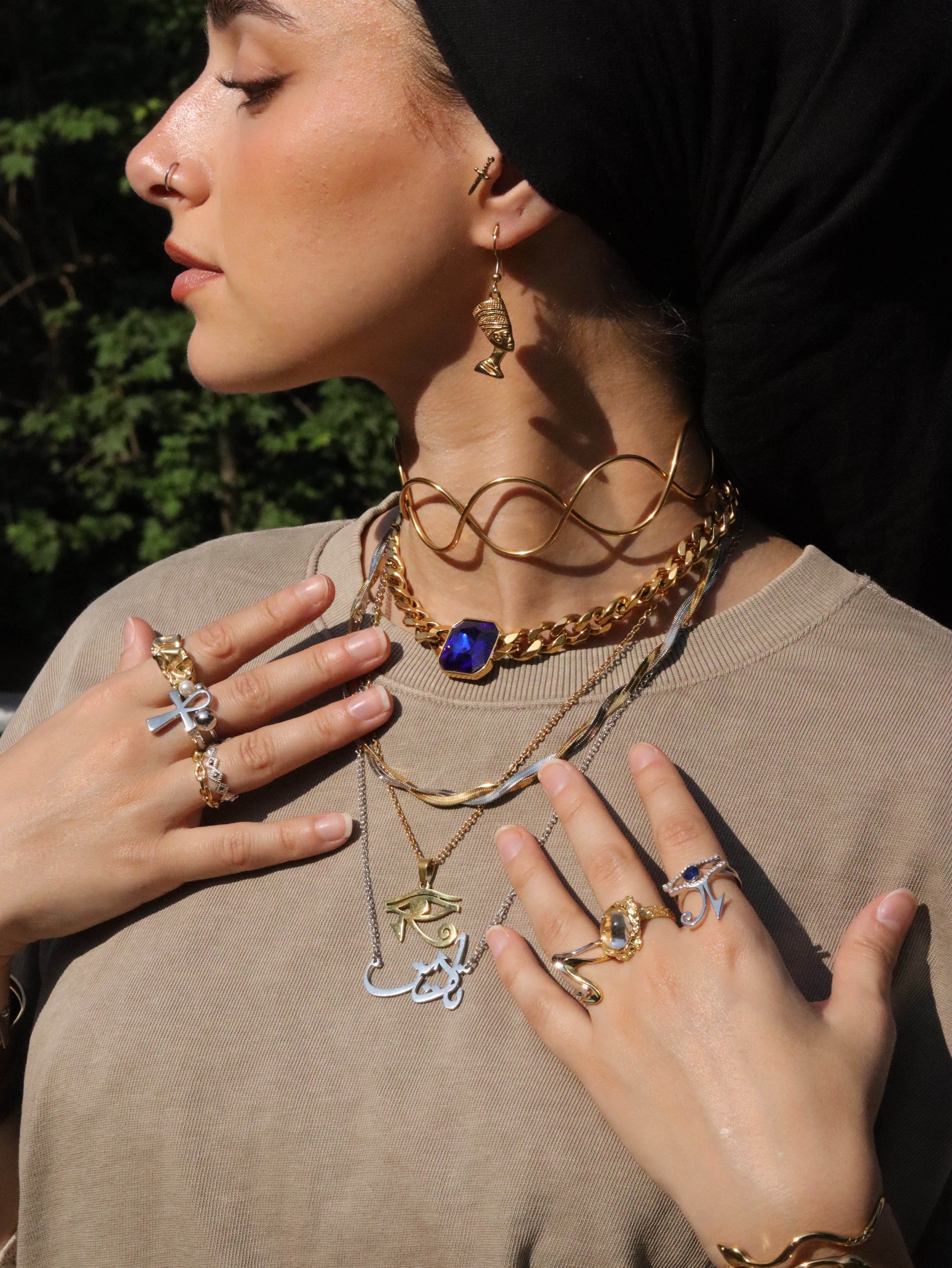 Woman in a black headscarf wearing a gold plated Arabic calligraphy name necklace layered with chains and symbolic pendants