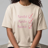 Model wearing a beige cotton T shirt with a pink Arabic checklist design featuring three lines of lettering from KIRO Clothing