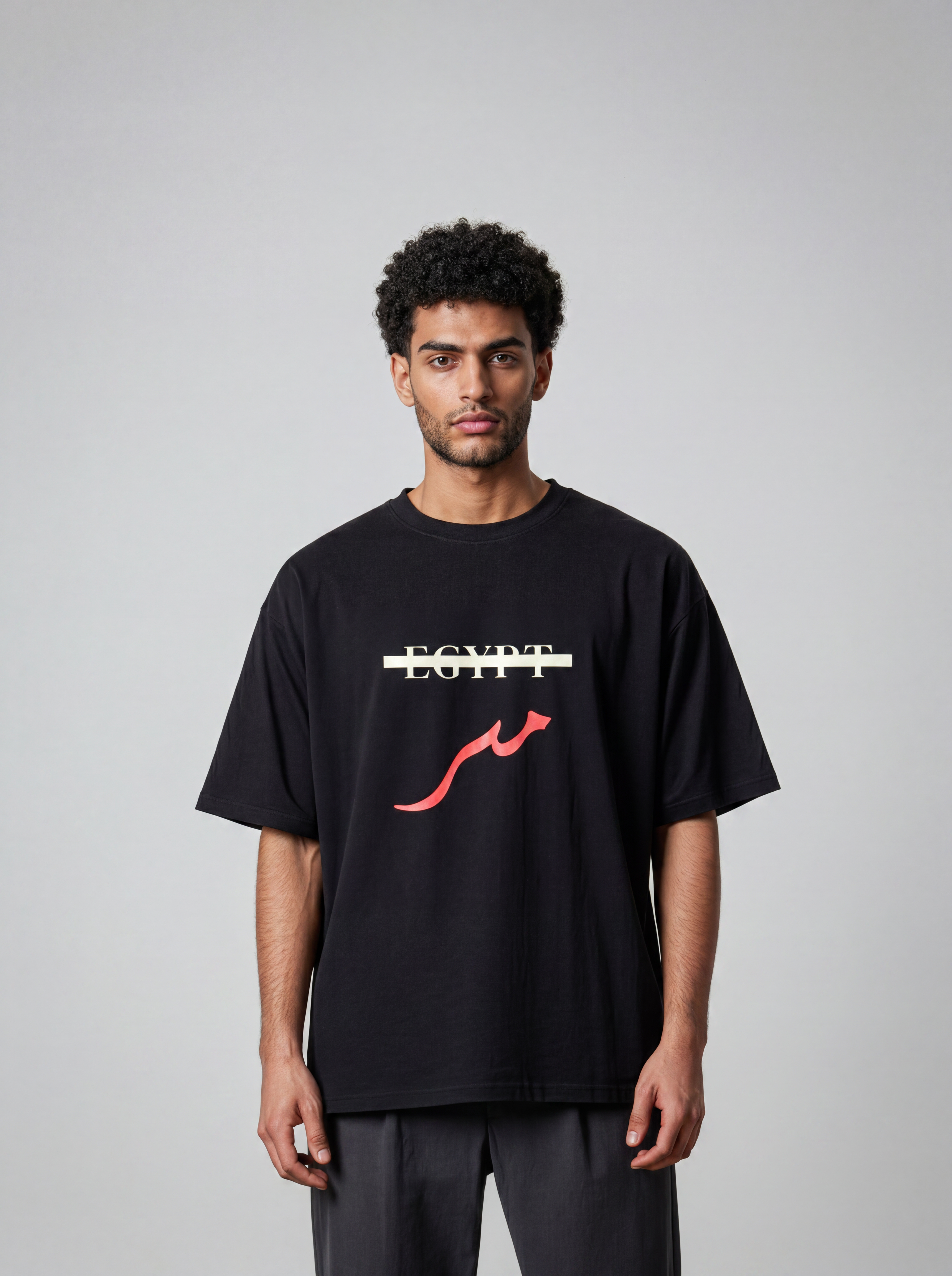 Male model wearing a black oversized cotton T shirt with the word Egypt crossed out and red Masr lettering on the front
