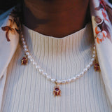 Woman wearing KIRO Scarab Pearl necklace, styled with a white top