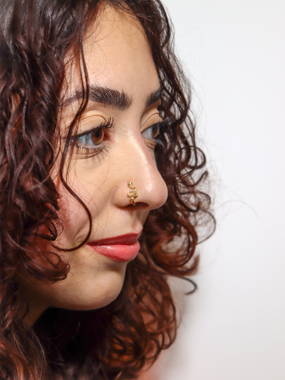 Close-up of a woman wearing a gold serpent faux nose ring, shown on the side of her nose. KIRO UK Nose Ring, Faux nose rings collection