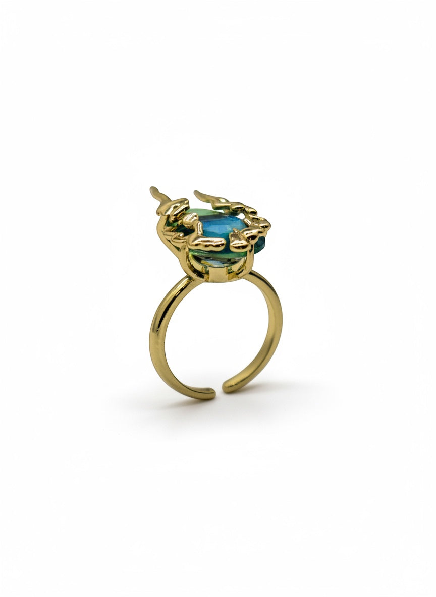 KIRO Amarna ring with a blue-green oval cubic zirconia gemstone set in 18K gold plated metal with unique claw-like details. Resizeable.