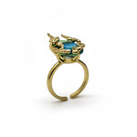 KIRO Amarna ring with a blue-green oval cubic zirconia gemstone set in 18K gold plated metal with unique claw-like details. Resizeable.