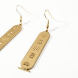 KIRO gold plated stainless steel drop earrings featuring oval cartouche pendants with engraved Egyptian hieroglyphs.
