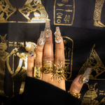 A hand wearing the Kiro Samer gold sunshine ring, paired with several other gold rings