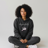 Woman wearing a black oversized hoodie with Respectfully and Arabic lettering on the front while seated cross legged KIRO Clothing collection