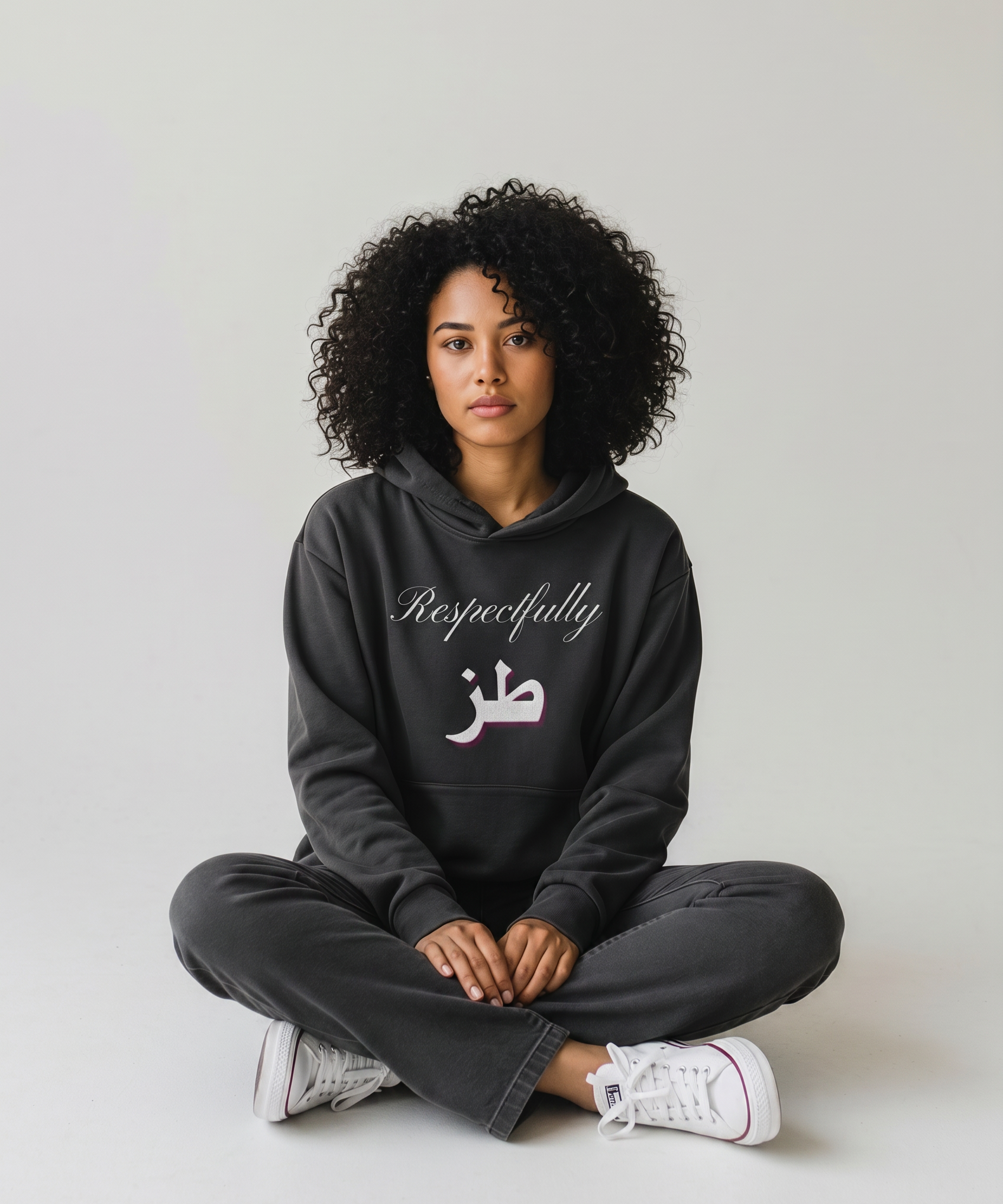 Woman wearing a black oversized hoodie with Respectfully and Arabic lettering on the front while seated cross legged KIRO Clothing collection