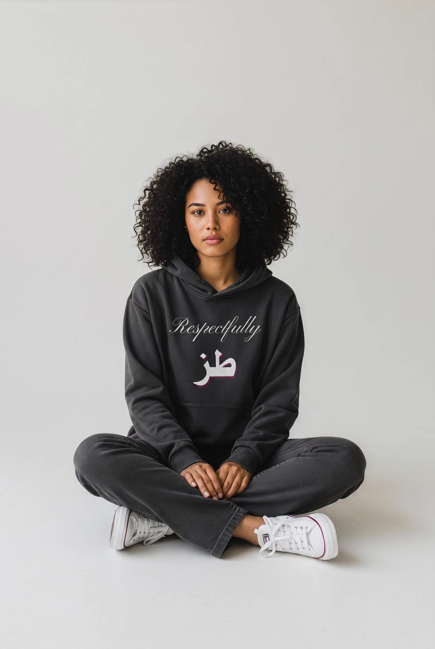 Woman wearing a black oversized hoodie with Respectfully and Arabic lettering on the front while seated cross legged KIRO Clothing collection