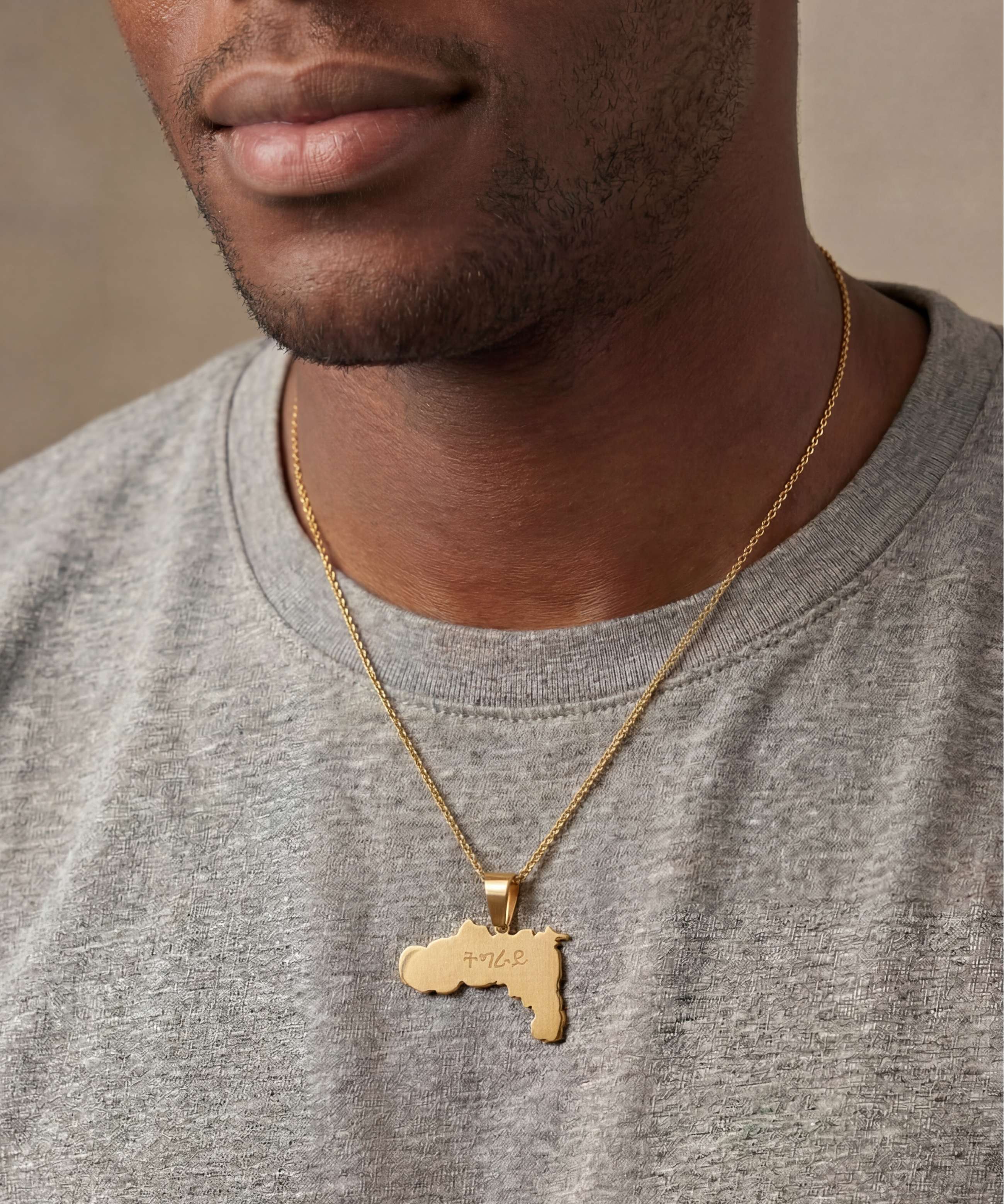 KIRO UK gold geometric Tigray map necklace worn over a gray shirt with a detailed pendant expressing cultural pride
