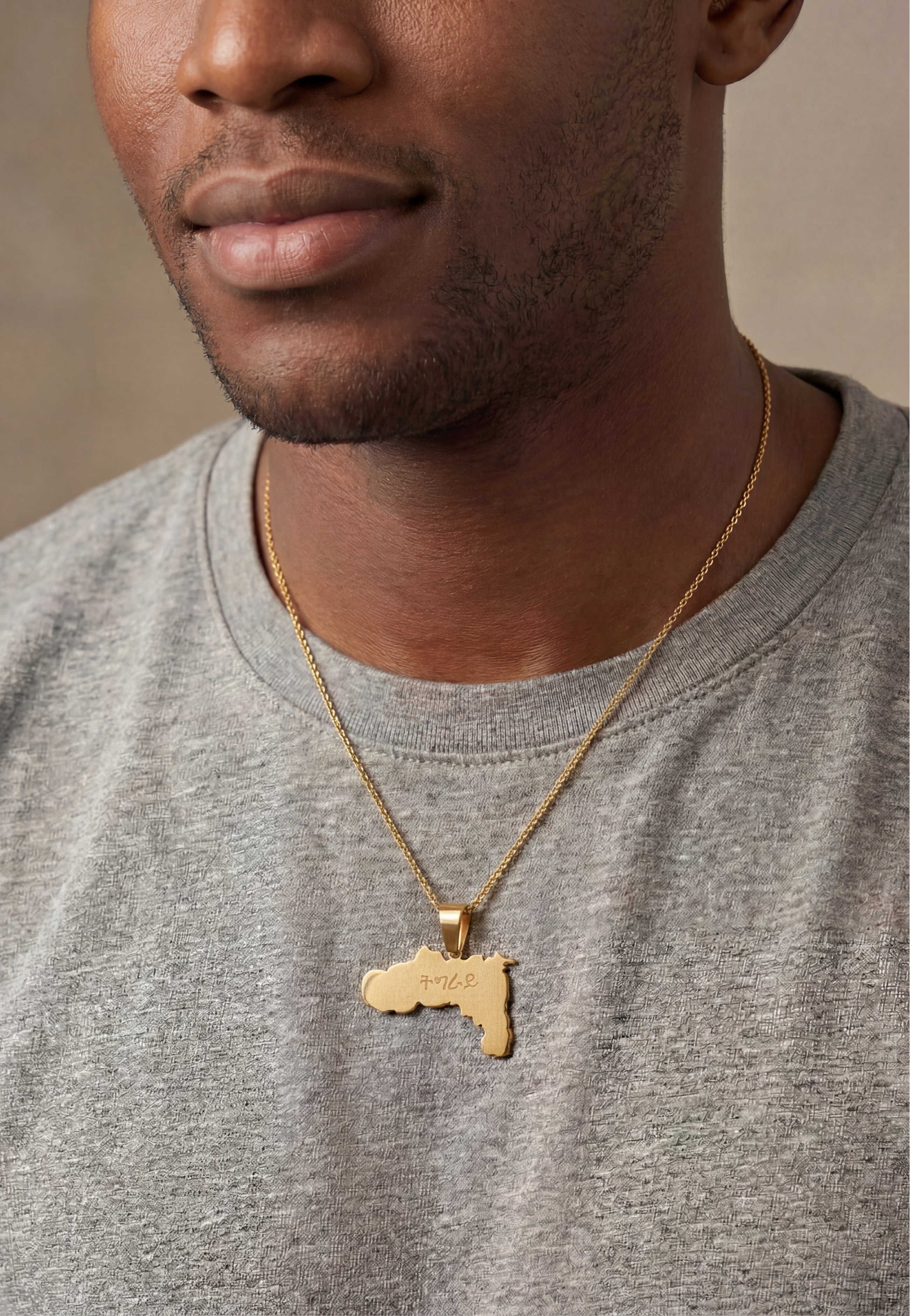KIRO UK gold geometric Tigray map necklace worn over a gray shirt with a detailed pendant expressing cultural pride